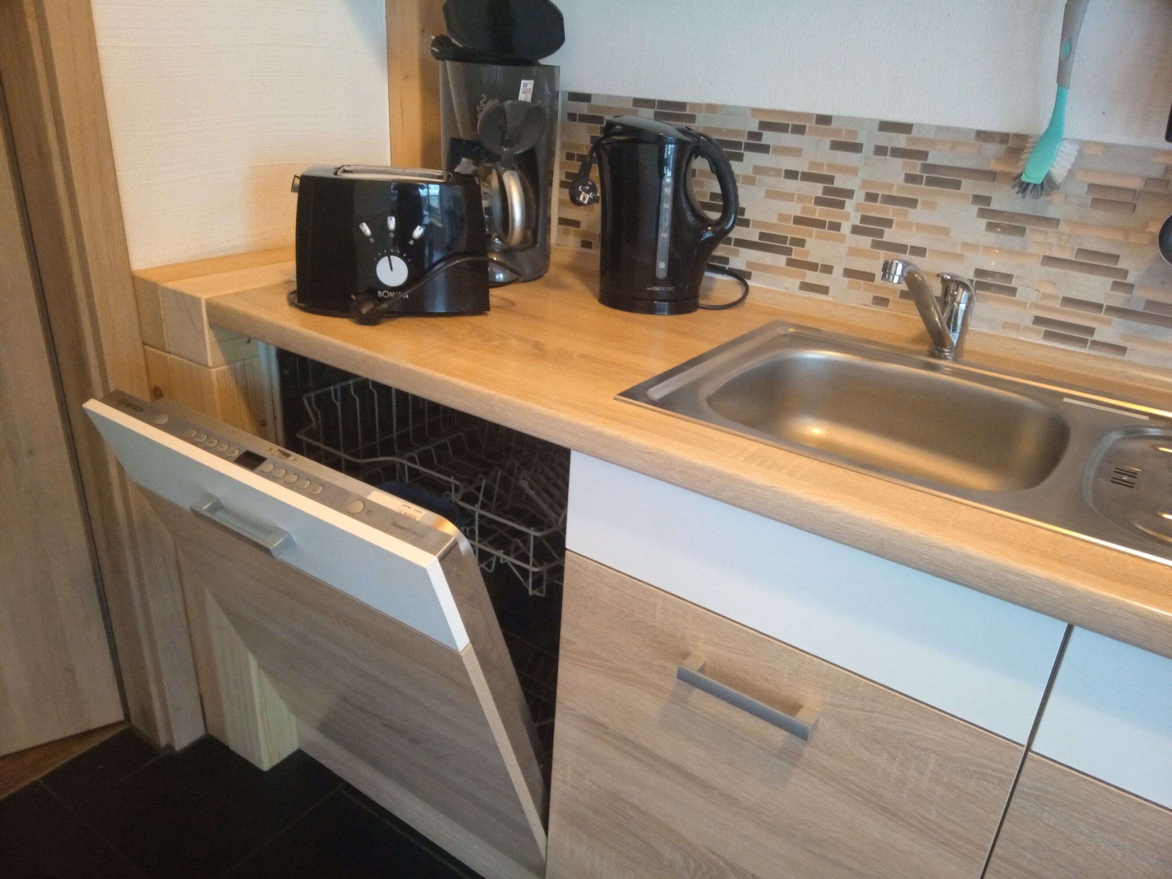Eine Küche mit Geschirrspüler, Kaffeemaschine, Wasserkocher und Spüle.