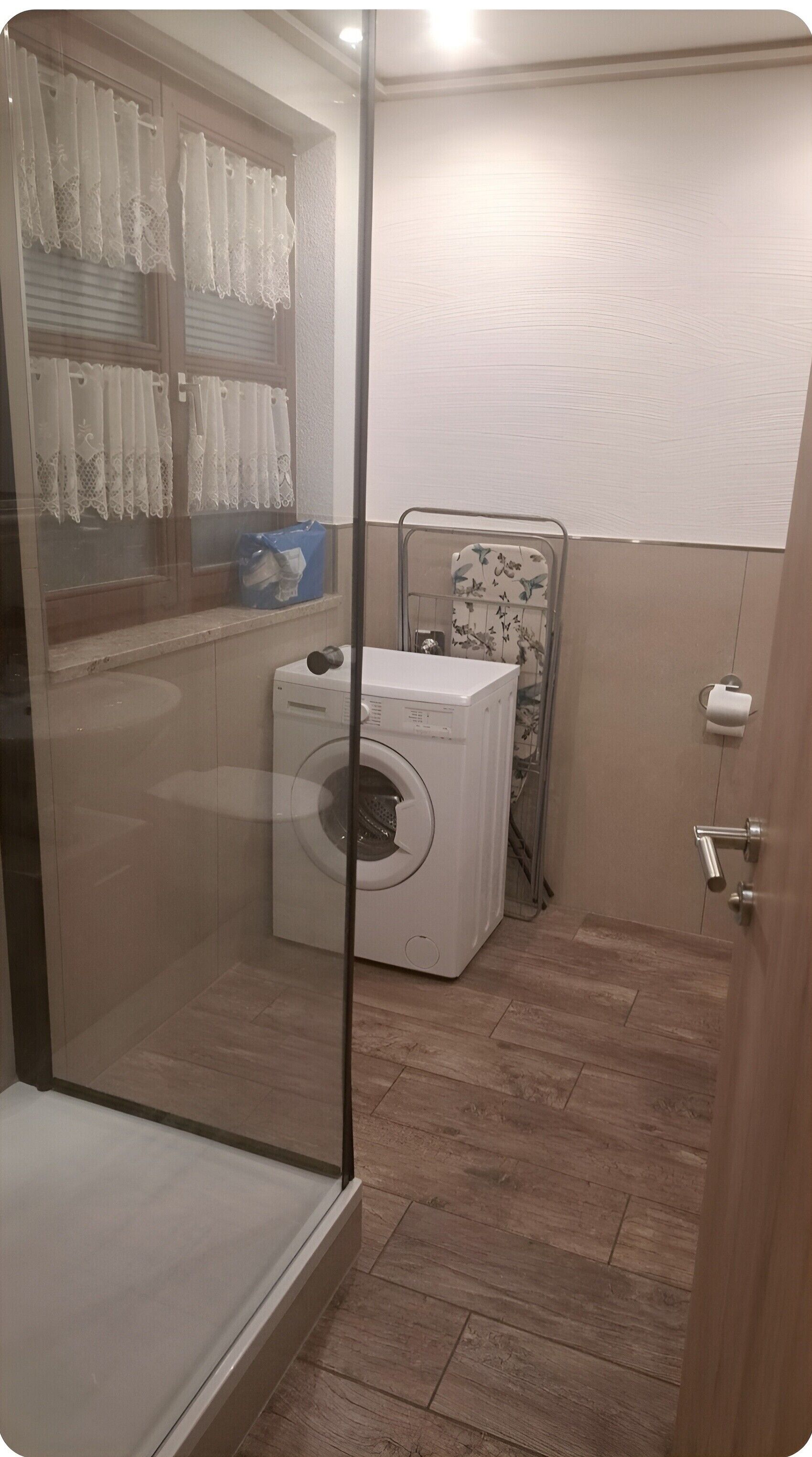 A bathroom with a glass shower enclosure, a washing machine, and a toilet.