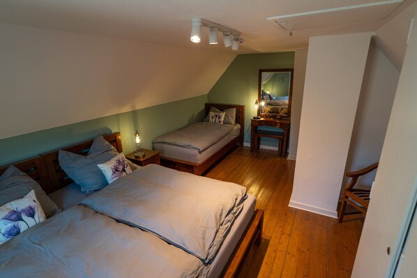 A bedroom with two beds, a wooden floor, a mirror, and a nightstand with a lamp.