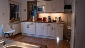 Een keuken met witte kastjes, een magnetron, een koffiezetapparaat en een koelkast.