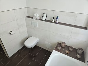 Un baño con inodoro, lavamanos, espejo y repisas con artículos de aseo.