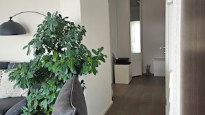 A modern living room with a large potted plant, a black sofa with blue cushions, and a black pendant lamp.