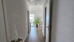 A hallway with wooden flooring, white walls, and a potted plant in the distance.
