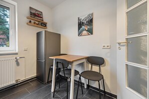 Une cuisine de taille réduite comprenant un réfrigérateur, une table en bois et deux chaises.