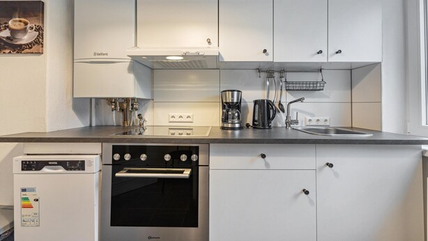 Una cocina moderna con armarios blancos, horno de acero inoxidable, lavavajillas y cafetera.