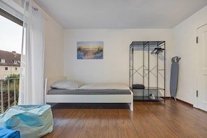 A bedroom with a bed, a painting, a metal storage unit, and a view of buildings outside. - Apartment 'Hannover Ogli' with Private Garden and Wi-Fi (Hannover)