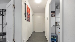 Un pasillo con armario, perchero, puerta y una pequeña zona de cocina con refrigerador y basurero.