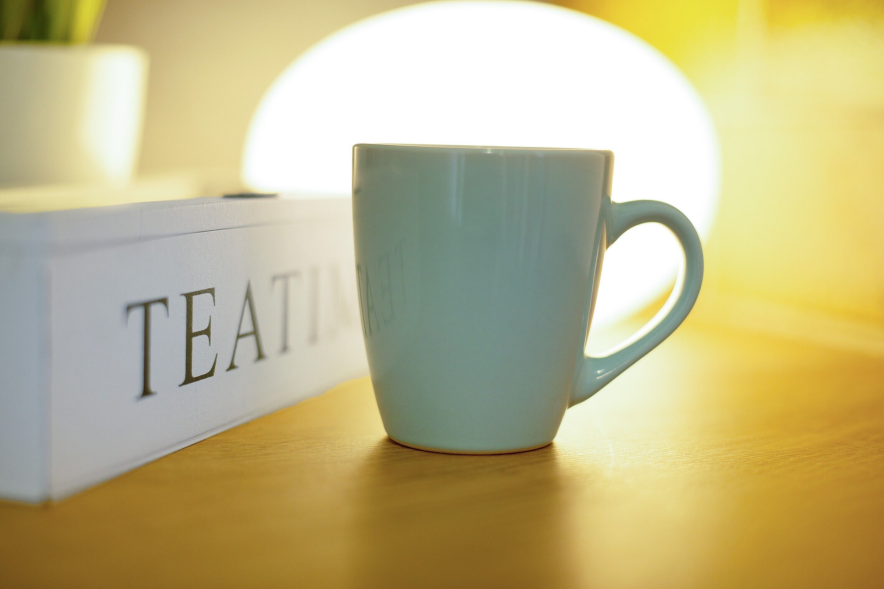A light blue mug on a wooden surface next to a white box with the word 'TEA' visible.