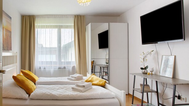 A hotel room with a bed, a desk, a television, and a window with curtains. - Seelina Apartment in Perach – Quiet, Cozy & Close to Nature (Perach)