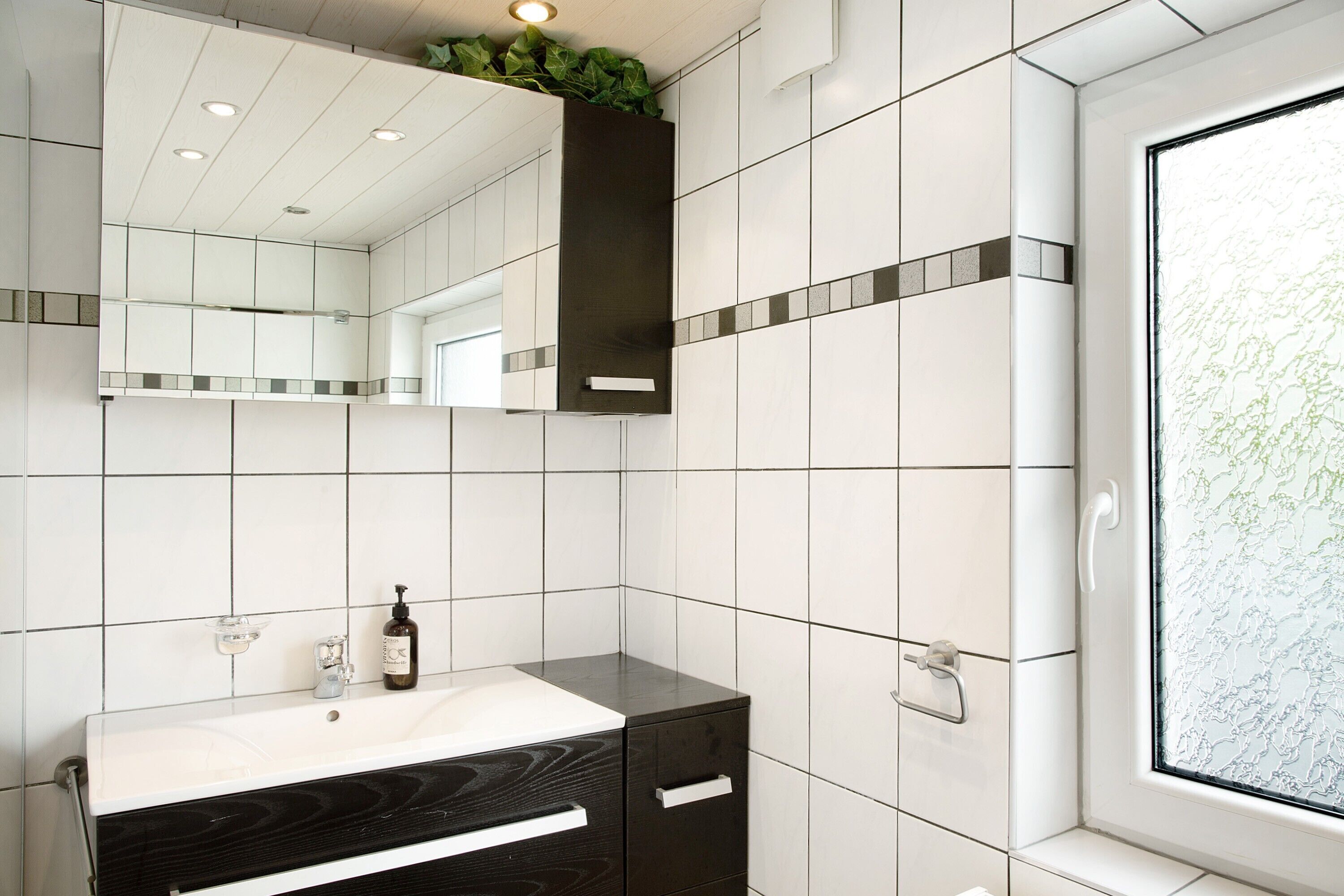 Une salle de bain avec des carreaux blancs, un meuble-lavabo noir, un miroir et une fenêtre donnant sur un beau paysage.