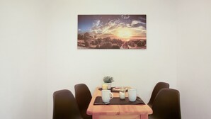 A dining area with a table set for two, a small potted plant, and a sunset painting on the wall. - Seelina Apartment in Perach – Quiet, Cozy & Close to Nature (Perach)