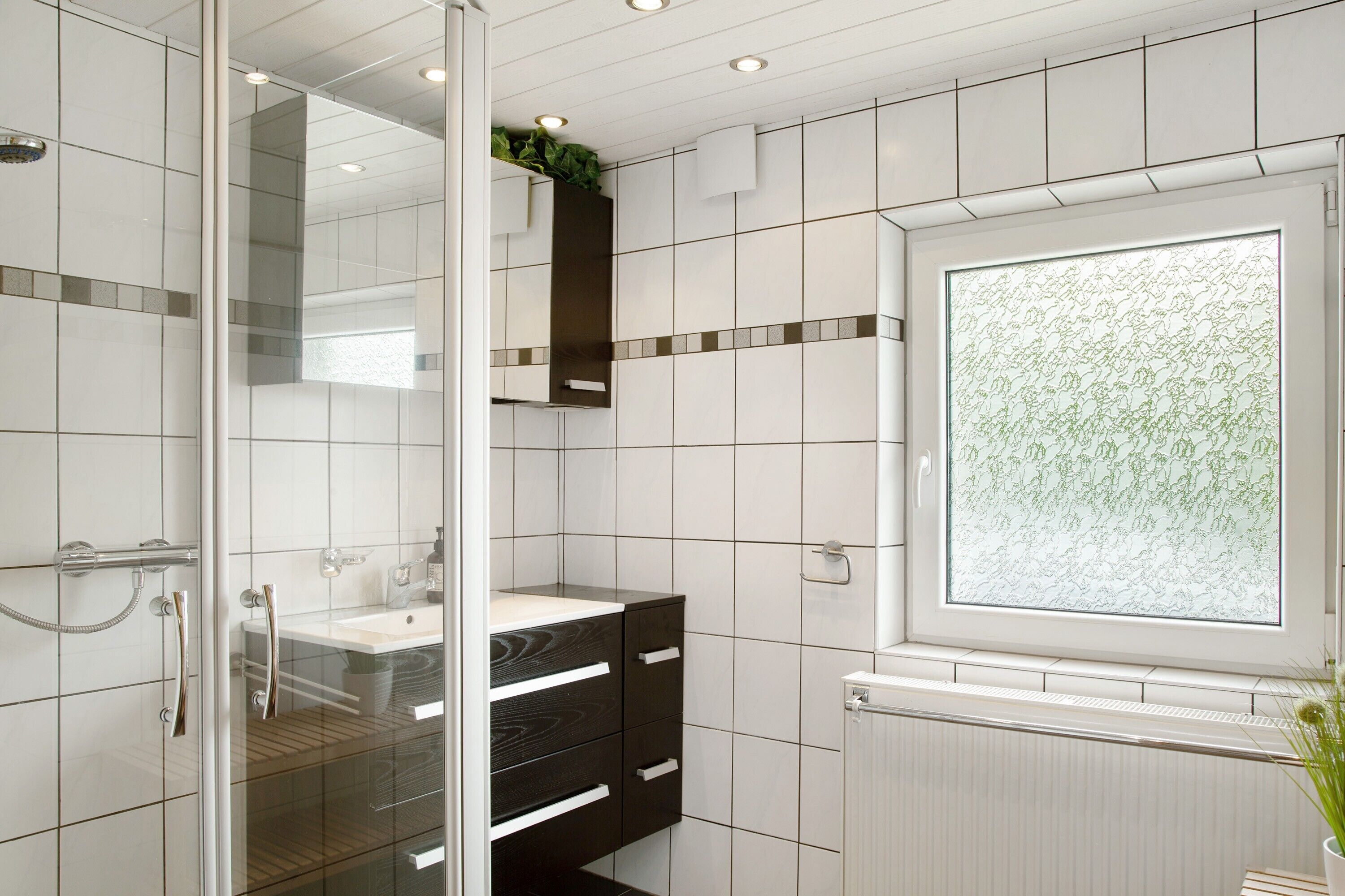 A bathroom with a glass shower enclosure, a sink with a mirror, and a window with a floral pattern.