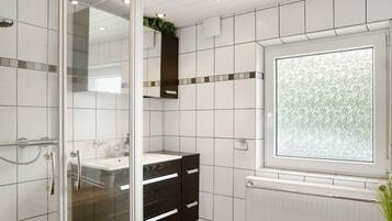 A bathroom with a glass shower enclosure, a sink with a mirror, and a window with a floral pattern.