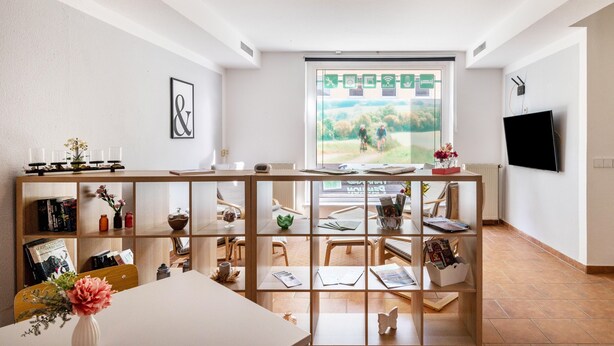 A modern living room with a large window, a flat-screen TV, and a wooden bookshelf.