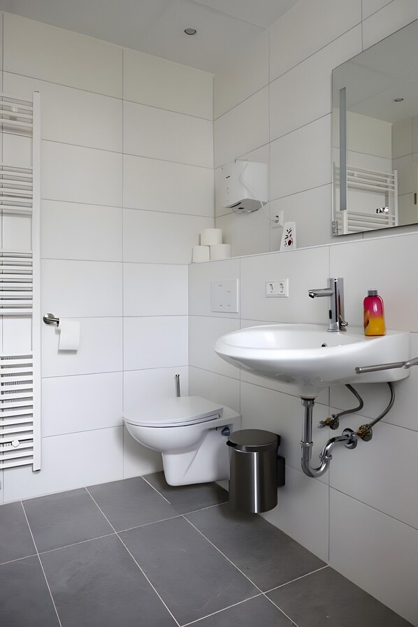 Un baño moderno con lavamanos, inodoro y ducha blancos.