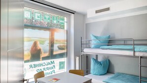 A bunk bed room with a table and chairs, a window with a view, and a poster on the window.