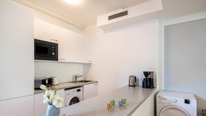 A compact kitchen with a microwave, toaster, and washing machine, a small sink, and a coffee maker.