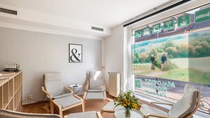A room with a large window, multiple chairs, a small table with a vase, and a framed sign on the wall.