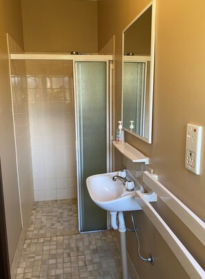 Un baño con ducha, lavamanos, espejo y repisas con artículos de aseo.