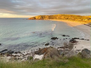 A coastal landscape with a sandy beach, rocky outcrops, and a hill with vegetation.