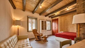 Ein Zimmer mit Holzboden, einer Couch, einem Massagesessel, einem Bett mit roter Decke und einem Tisch.