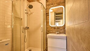 Ein Badezimmer mit einer gläsernen Dusche, einem weißen Waschbecken und einem beleuchteten Spiegel.