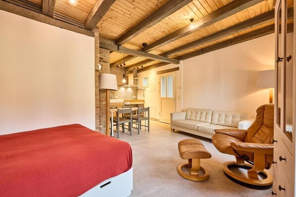 A bedroom with a bed, a wooden rocking chair, a sofa, and a dining area with chairs and a table.