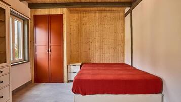 Un dormitorio con techo de madera, colcha roja, armario y ventana.