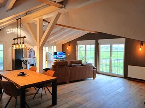 A spacious loft-style room with a wooden dining table, a sofa, and a television. - Country House 'Hof Sorgenfrei' with Mountain View, Wi-Fi and Air Conditioning (Buch)