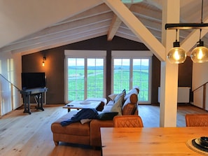Ein geräumiges Zimmer mit großem Fenster, einem Holzesstisch, einer Couch und einem Fernseher.