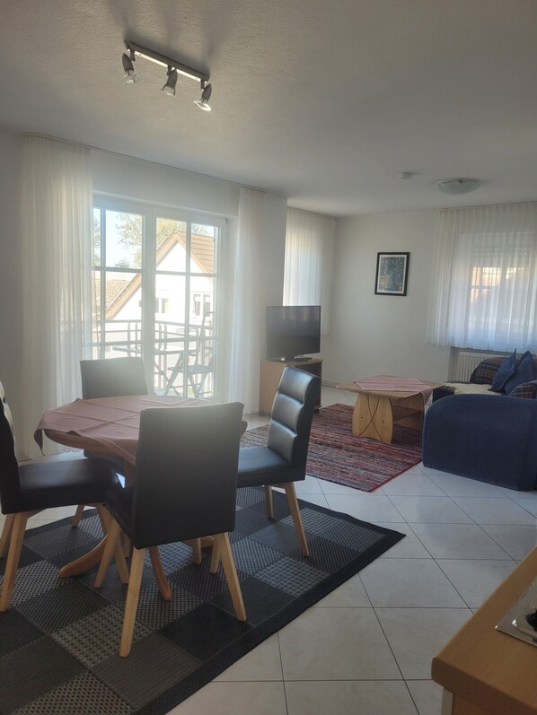 A living room with a dining table, chairs, a TV, a sofa, and a window with curtains.