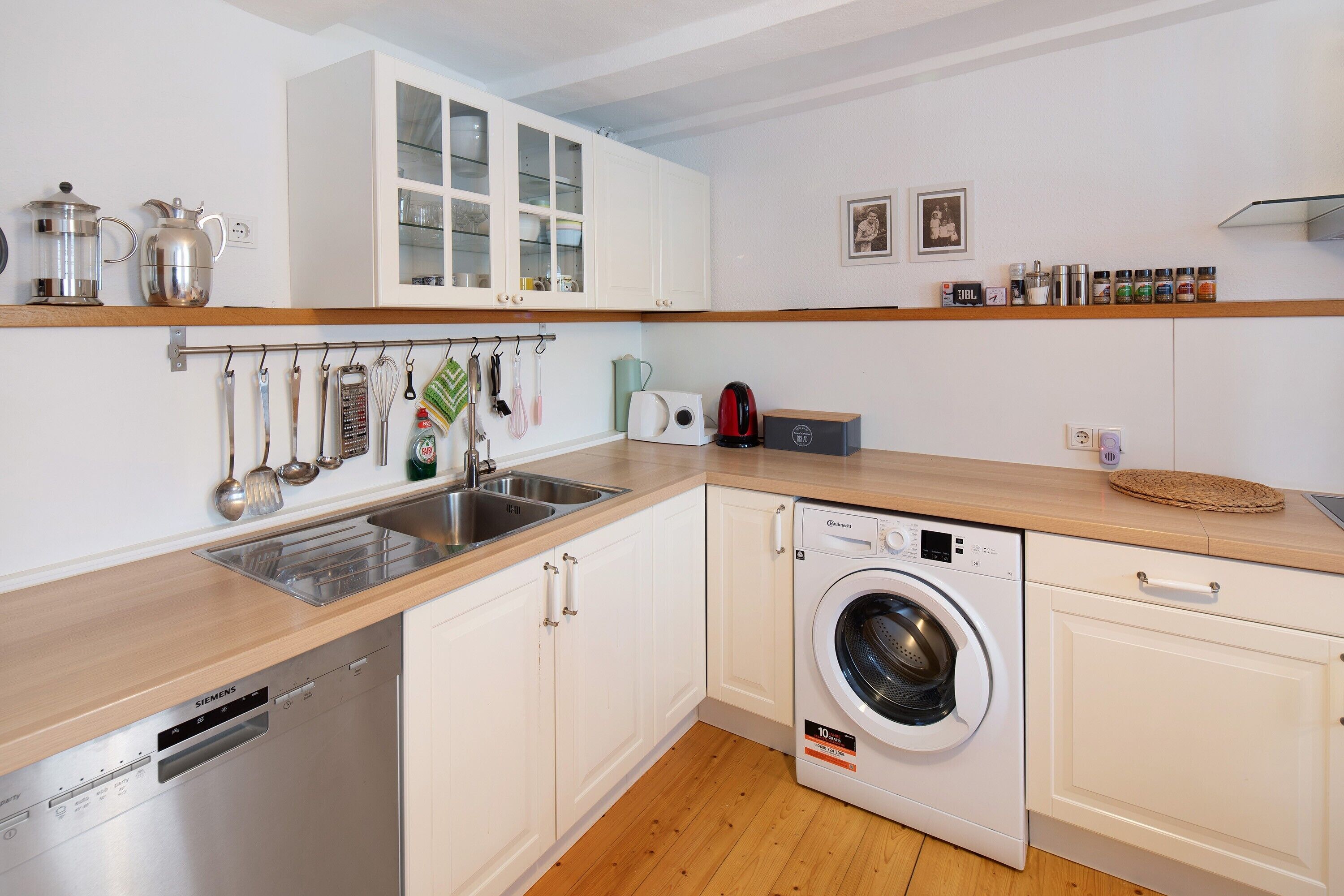 A modern kitchen with white cabinets, a dishwasher, a washing machine, and various kitchen utensils.