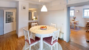 Een eetgedeelte met een ronde tafel, witte stoelen en een schaal fruit.