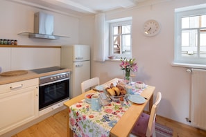 A kitchen with a stove, oven, and a dining table set with plates, cups, and a vase of flowers. - Apartment 'Omi Anni' with a view of the market square, Private Terrace and Wi-Fi (Schlitz)