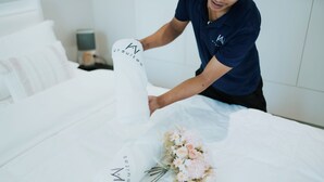 Een hotelkamer met een netjes opgemaakt bed, een bedlamp en een bloemenboeket.