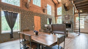 Interior de una cabaña de troncos con una pared de piedra, muebles de madera, una chimenea y una escalera.