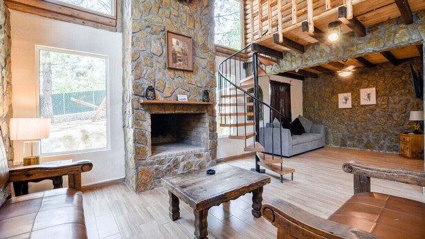 Una chimenea de piedra, muebles de madera, una escalera y un muro de piedra.