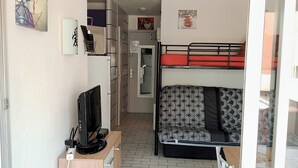 A compact living space with a bunk bed, a small kitchenette, a TV, and a foldable chair.