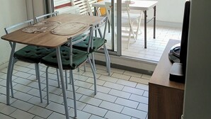 A dining area with a table and chairs, a sliding glass door leading to a balcony, and a refrigerator in the corner.