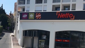 A multi-story building with a Netto supermarket on the ground floor, adjacent to a road with a sidewalk.