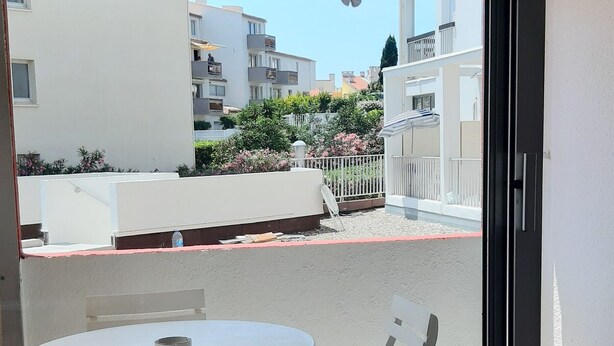 A balcony with a white table and chairs, a view of neighboring buildings, and a butterfly decoration on the ceiling.