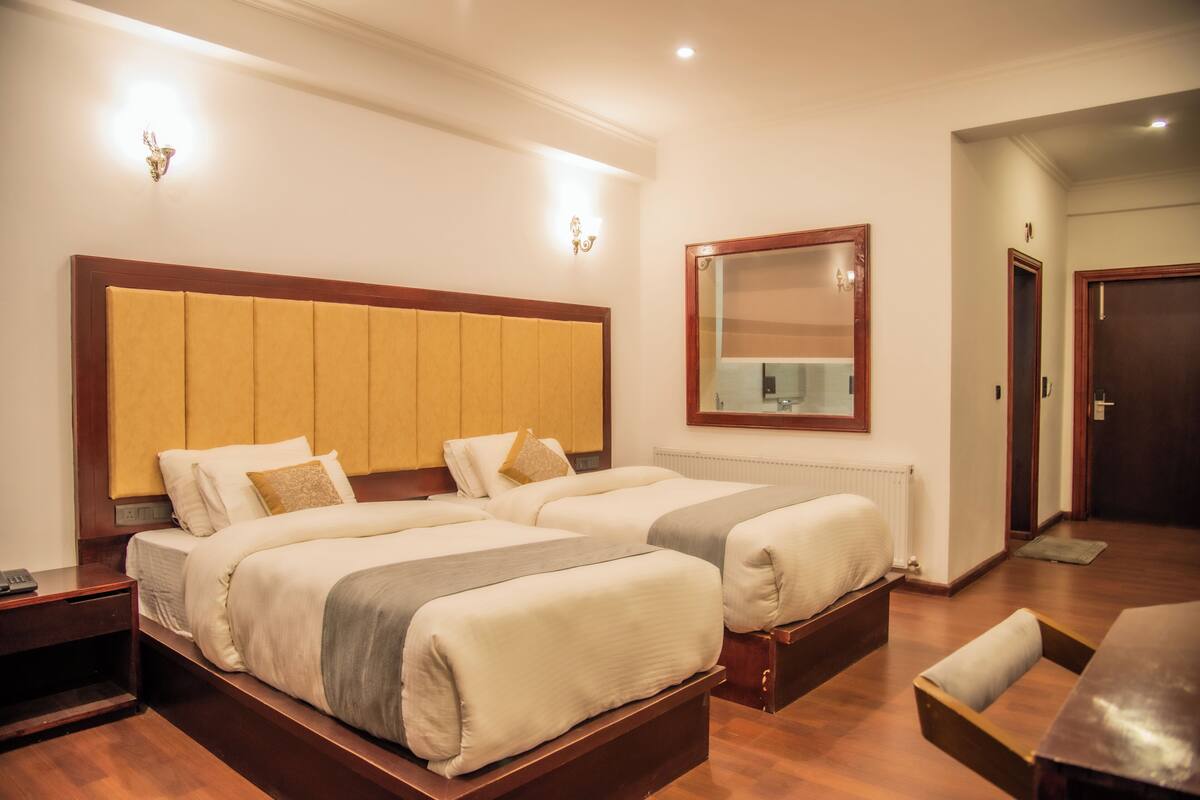 Ein Hotelzimmer mit zwei Betten, einem Holz-Kopfteil, einem Spiegel und einer hölzernen Bank.