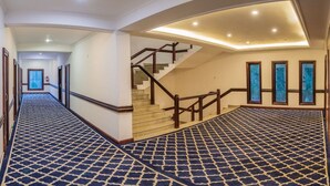 A hotel hallway with a patterned carpet, a staircase with wooden railings, and framed artwork on the walls. - Hotel Zomday (Leh)