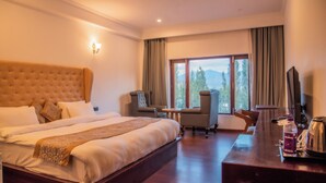 A hotel room with a large bed, a desk, and a chair. There is a window with a view of trees and mountains. - Hotel Zomday (Leh)