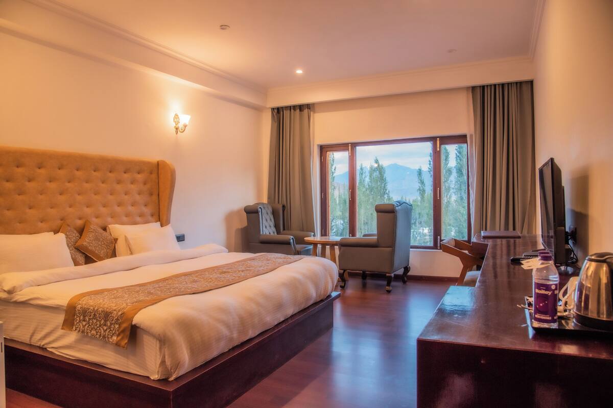 Ein Hotelzimmer mit einem großen Bett, einem Schreibtisch und einem Stuhl. Ein Fenster bietet Blick auf Bäume und Berge.