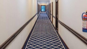A hotel hallway with a patterned carpet, doors on both sides, and a fire extinguisher on the right wall. - Hotel Zomday (Leh)