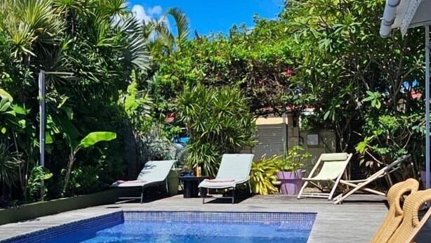 A clear blue pool with lounge chairs and tropical plants.