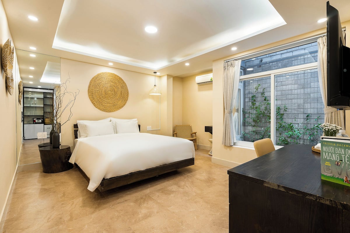 A modern bedroom with a large bed, a desk, and a window with a view of greenery.
