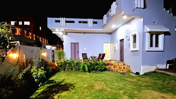 Una casa moderna de dos pisos con un césped cuidado y un pequeño patio con mobiliario exterior.