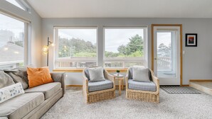 A cozy living room with a sofa, two wicker chairs, a small table, and a door leading outside. - Ocean Views, Game Garage & Steps to Neahkahnie Beach | Bella Sol by AvantStay (Nehalem)
